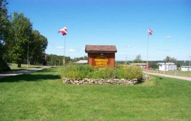 The Ponderosa Campsite entrance sign with American and Canadian flags flying over a stone flower bed.